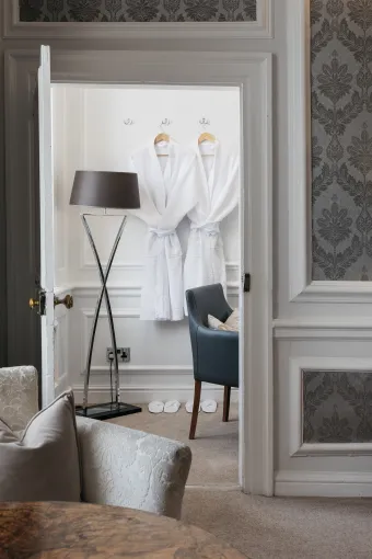 Dressing gowns hanging on the wall beyond a door with a chair and a lamp in front