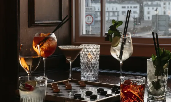 A selection of drinks and a game of Draughts on a table by a window in The Kingsley Lounge at The Royal Hotel Bideford