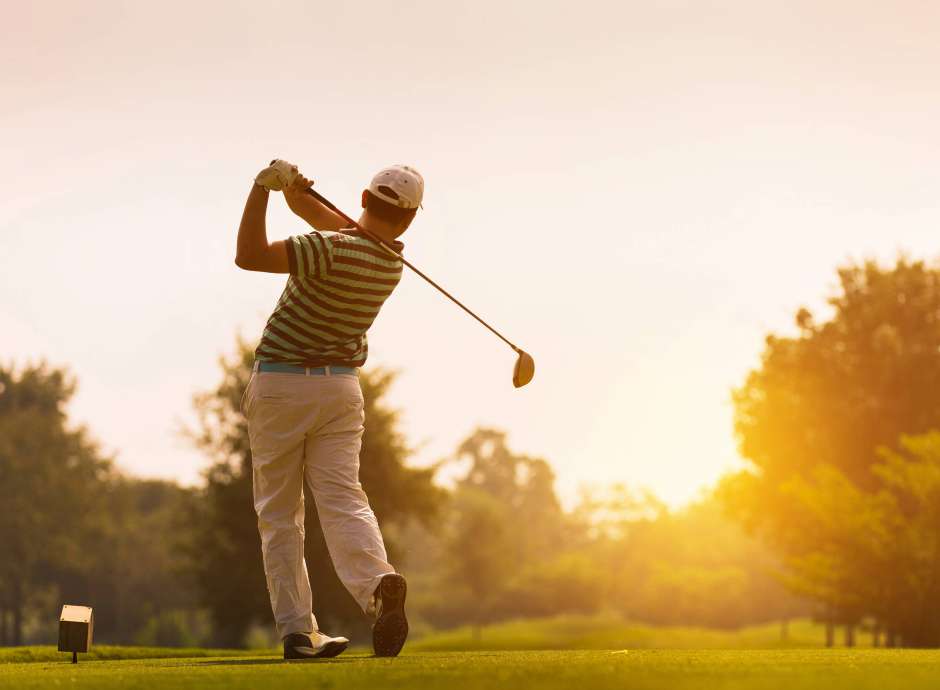 Man playing gold with sunsetting in distance
