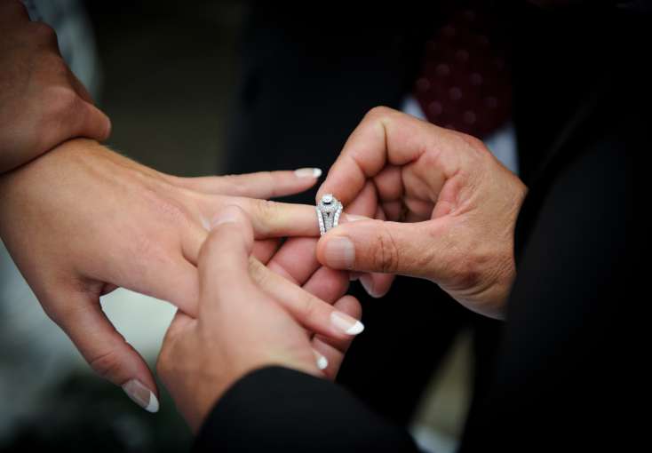groom putting wedding ring on finger of bride
