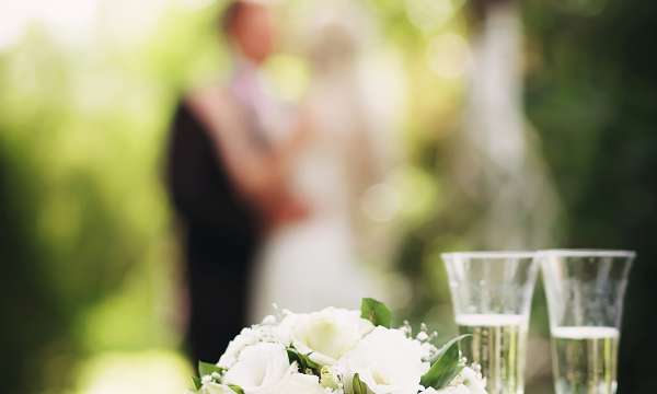 Bouquet and champagne on table with bride and groom in background